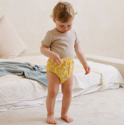 Petit enfant debout portant une culotte d’apprentissage lavable jaune avec motifs soleil, dans une chambre lumineuse